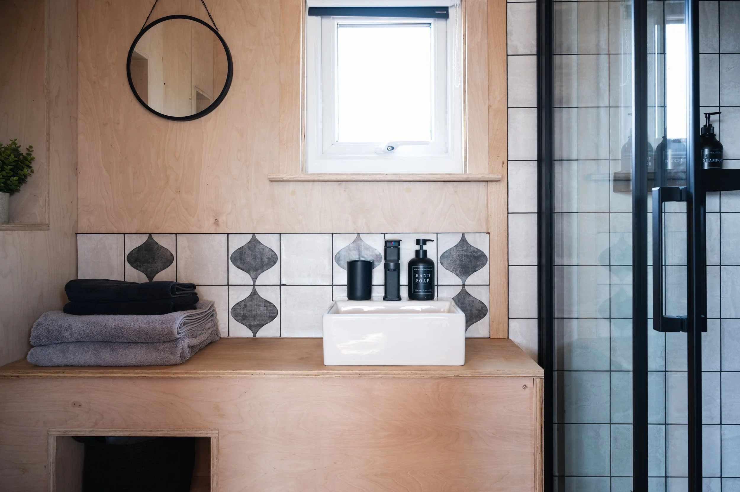 Stylish tiny home bathroom inside an off-grid cabin, with tiled shower, compact sink, and natural plywood interior design.