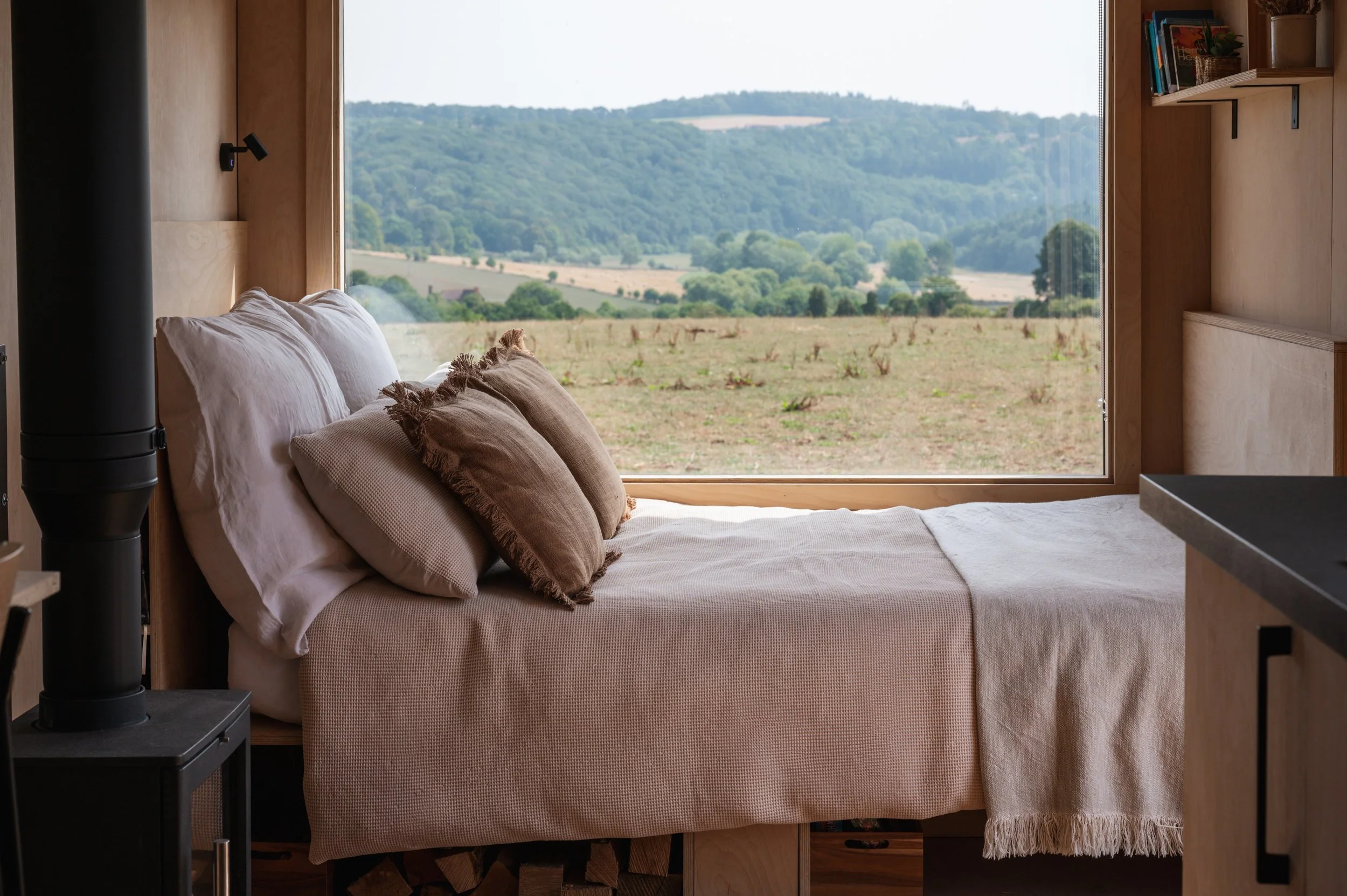 Wake up to breathtaking countryside views from a cosy tiny house bed. This modern cabin combines natural wood interiors, soft linen bedding, and a log burner for the ultimate escape in nature.