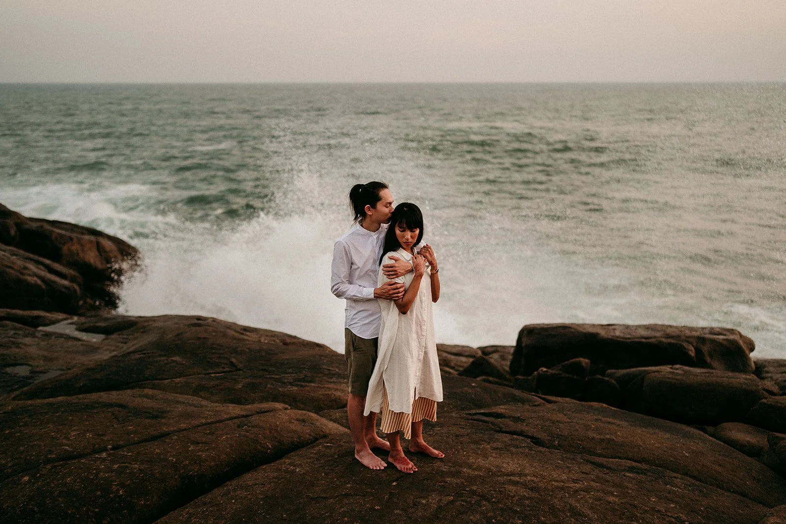 Romantic couple embracing on a rocky shore at sunset.