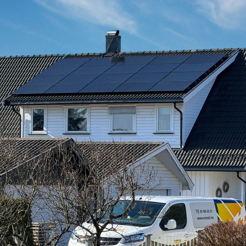 Hus med solcellepaneler på taket og en hvit tjenestebil parkert foran.