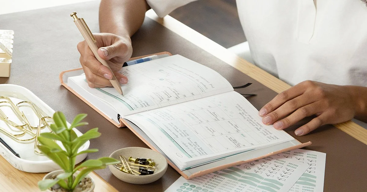 Woman writing in planner in modern desk setting.