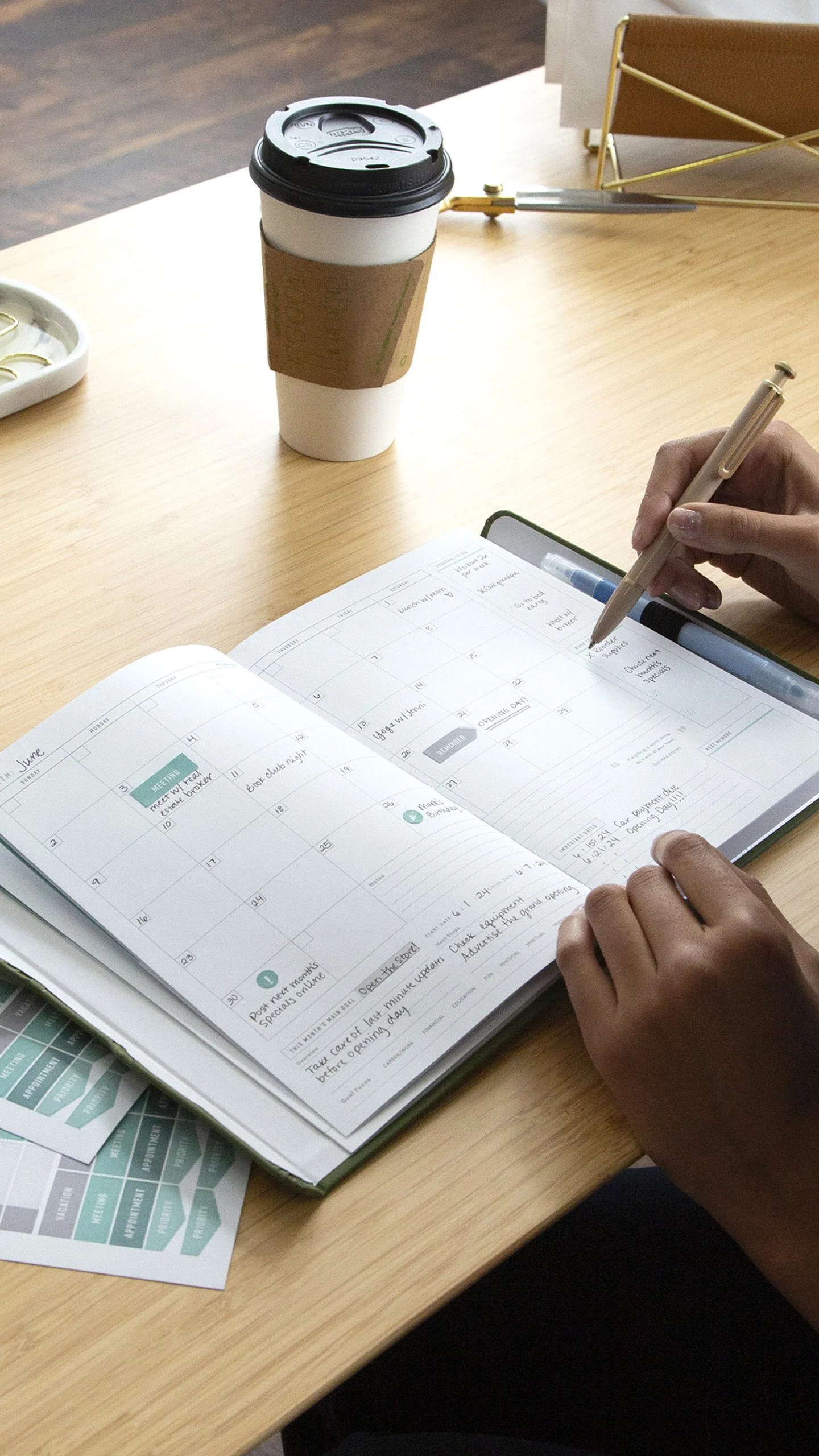 Woman writing in FOUNDATION planner on modern desk setting.