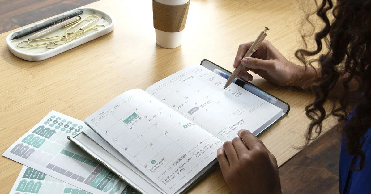 Woman writing in FOUNDATION planner on modern desk setting.