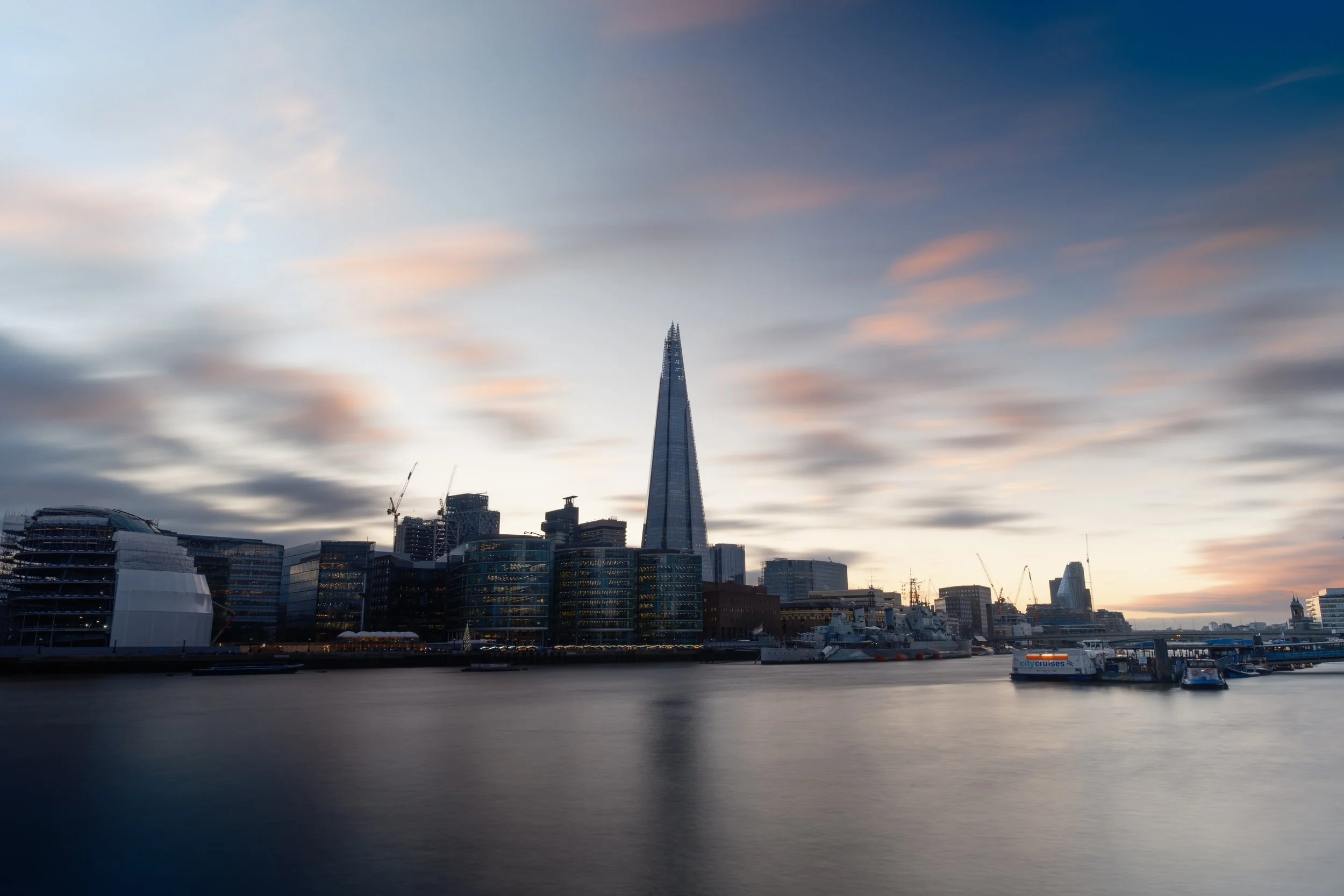 Skyline of London with The Shard skyscraper at sunset over the Thames River.