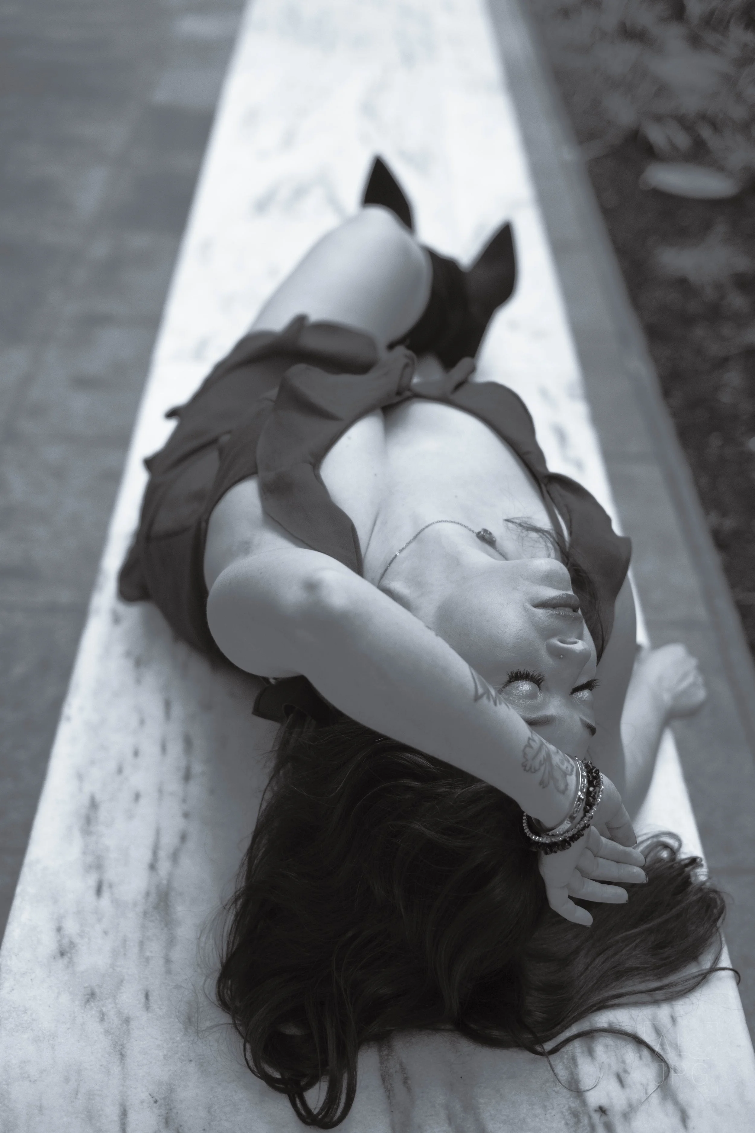 A young woman lying down on her back on a stone bench with her eyes closed, wearing a sleeveless top, shorts, jewelry, and a necklace, and resting her head on her arm.