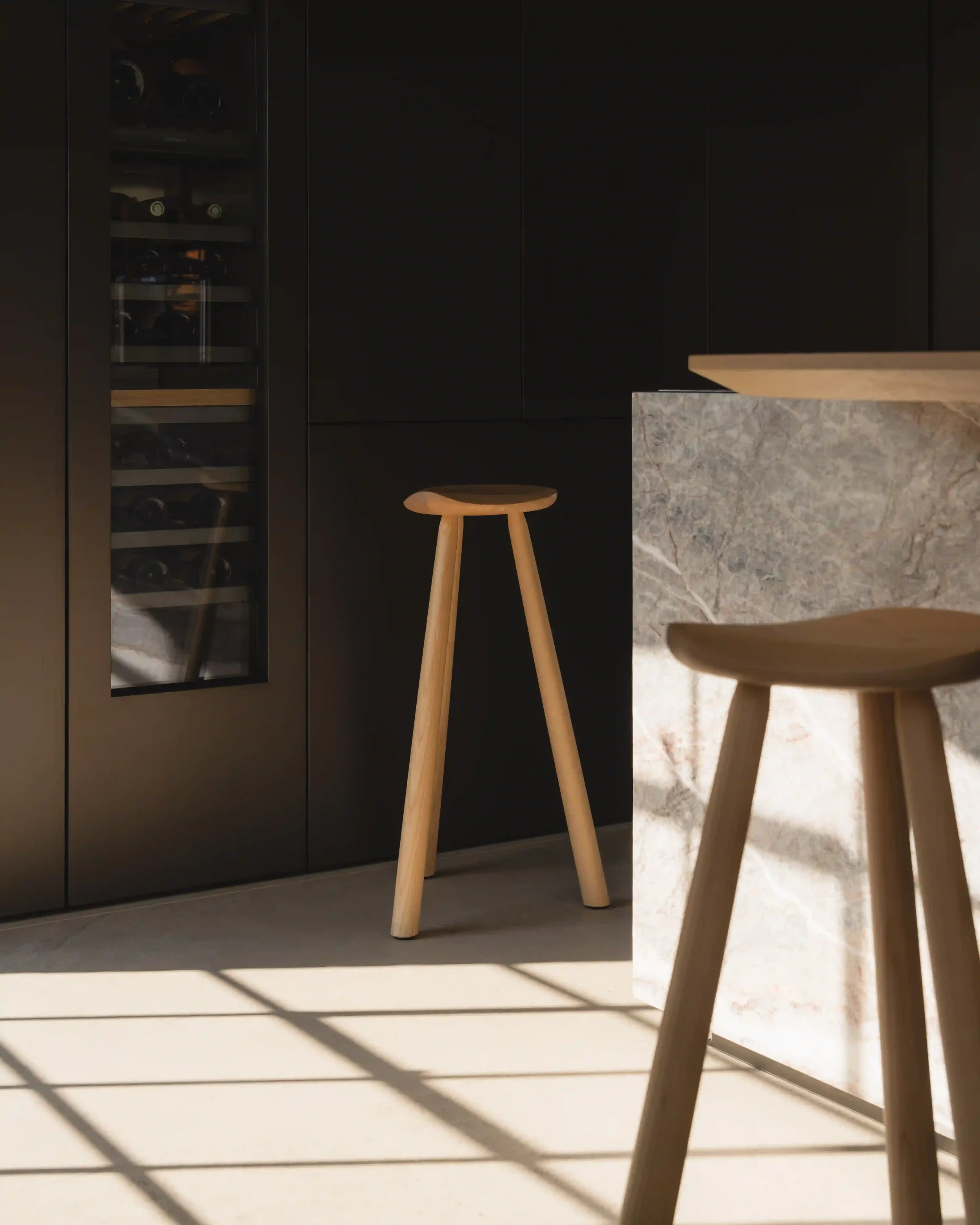 Close-up of a modern kitchen with black cabinets, a marble island, and light wooden stool. Designed by abitalia south coast across wider UK.