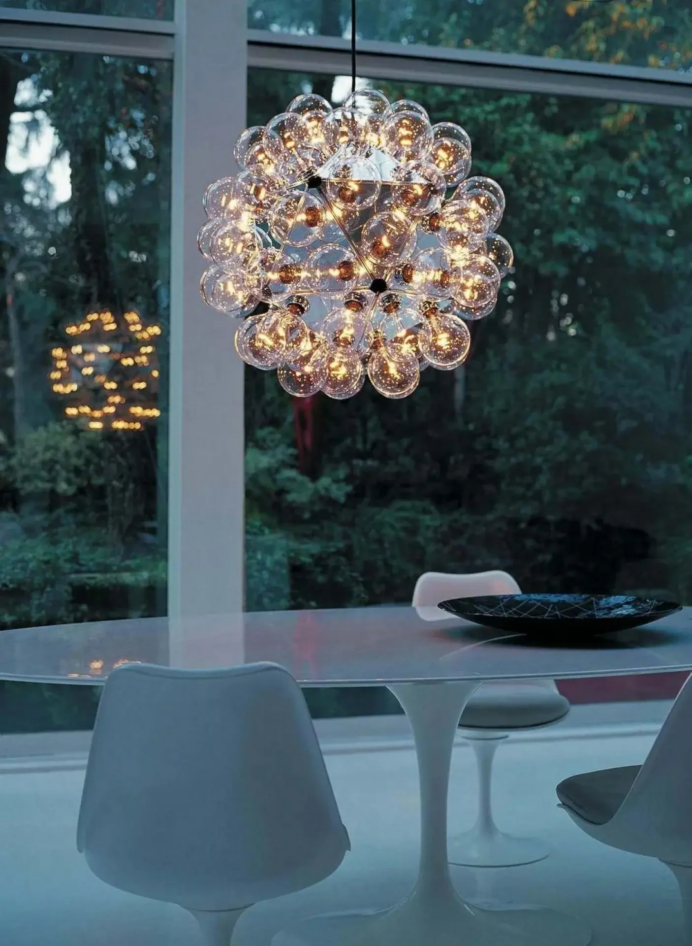 Taraxacum 88 chandelier shown suspended in an open interior, highlighting its sculptural form and constellation of exposed bulbs emitting a warm ambient glow.
