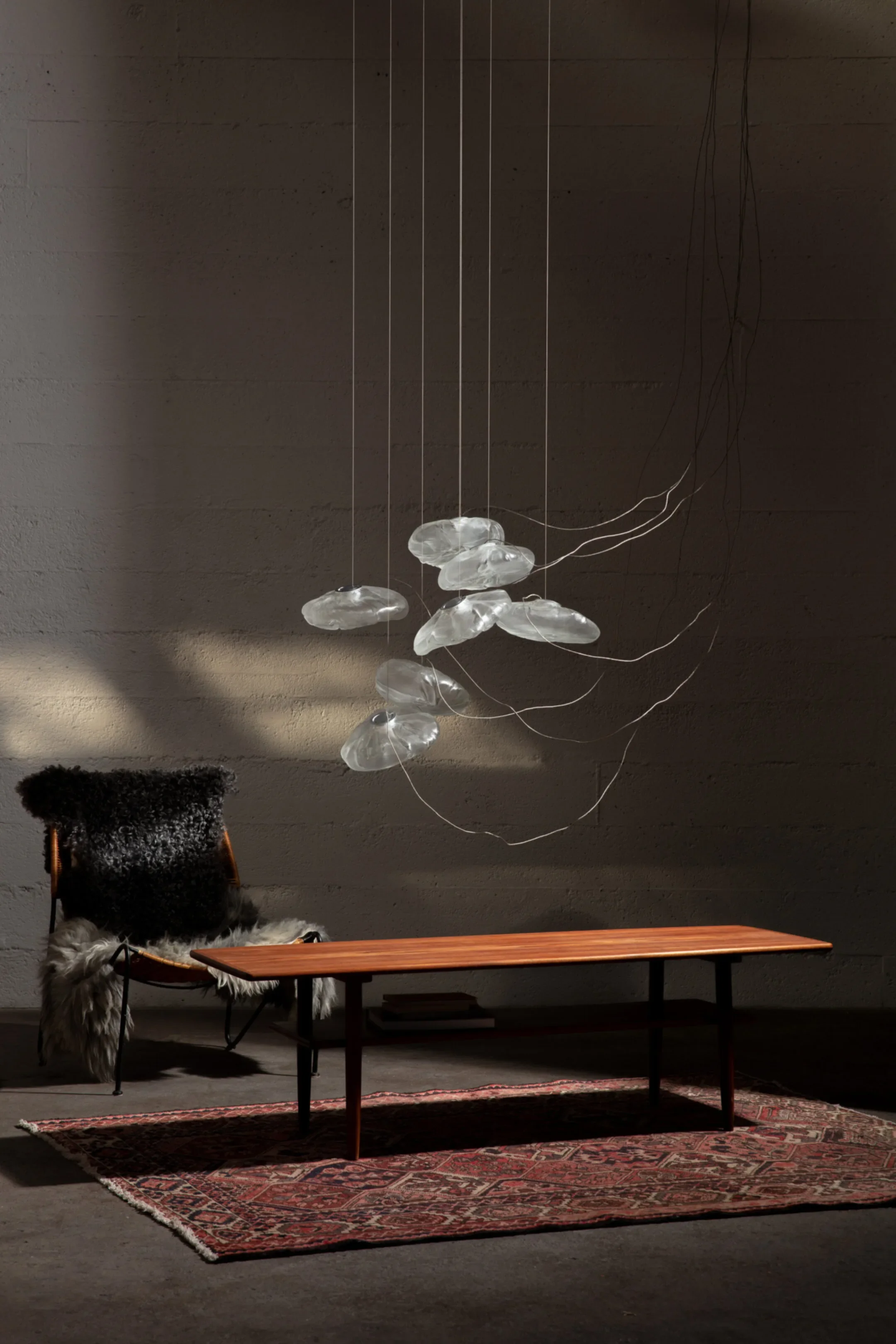 Minimalist interior with a wooden coffee table on a patterned rug, a black chair with a fur throw, and a hanging glass sculpture