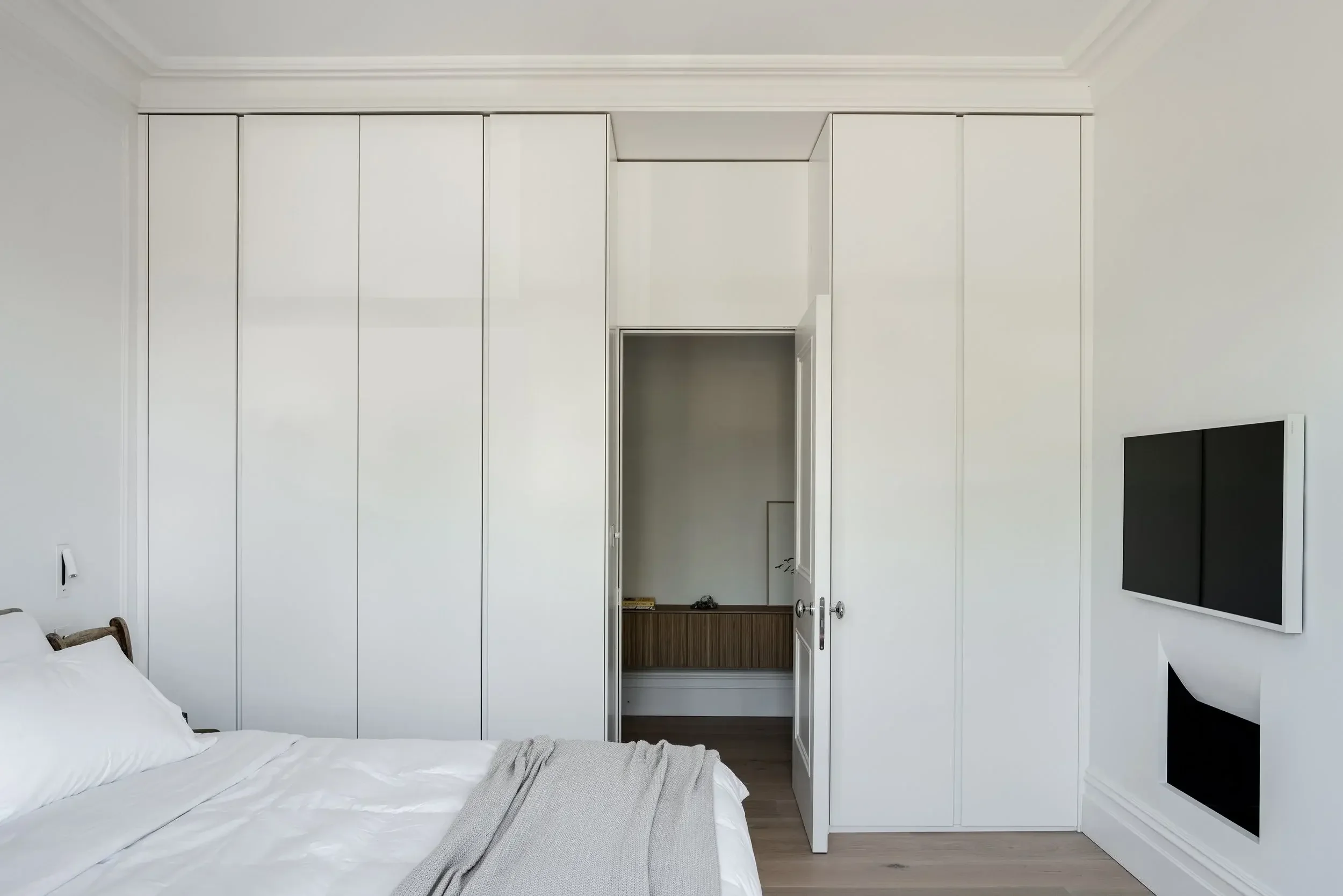 Bespoke floor-to-ceiling white gloss wardrobe by Abitalia South Coast in Poole, seamlessly integrated around a bedroom doorway.
