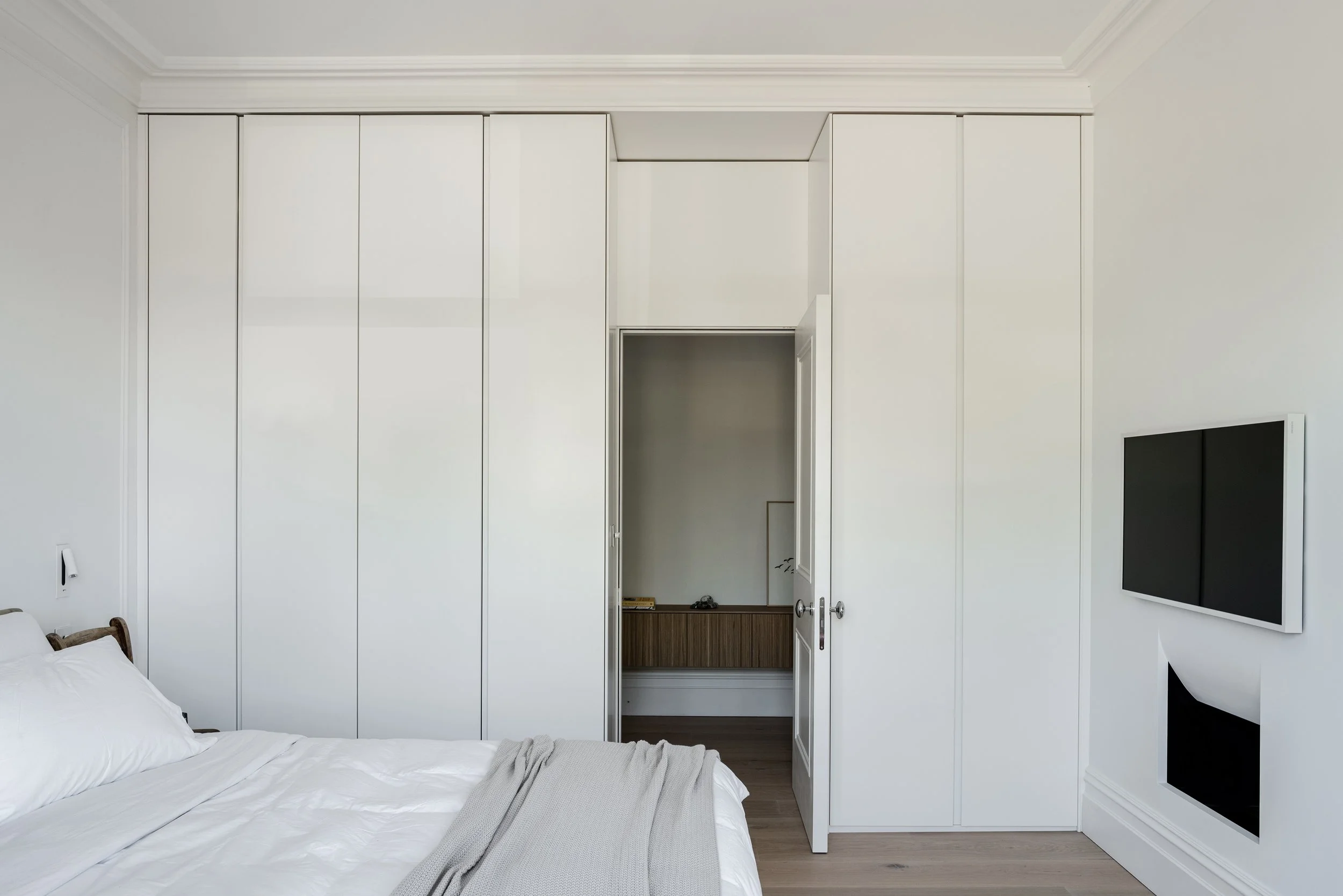 Bespoke floor-to-ceiling white gloss wardrobe by Abitalia South Coast in Poole, seamlessly integrated around a bedroom doorway.