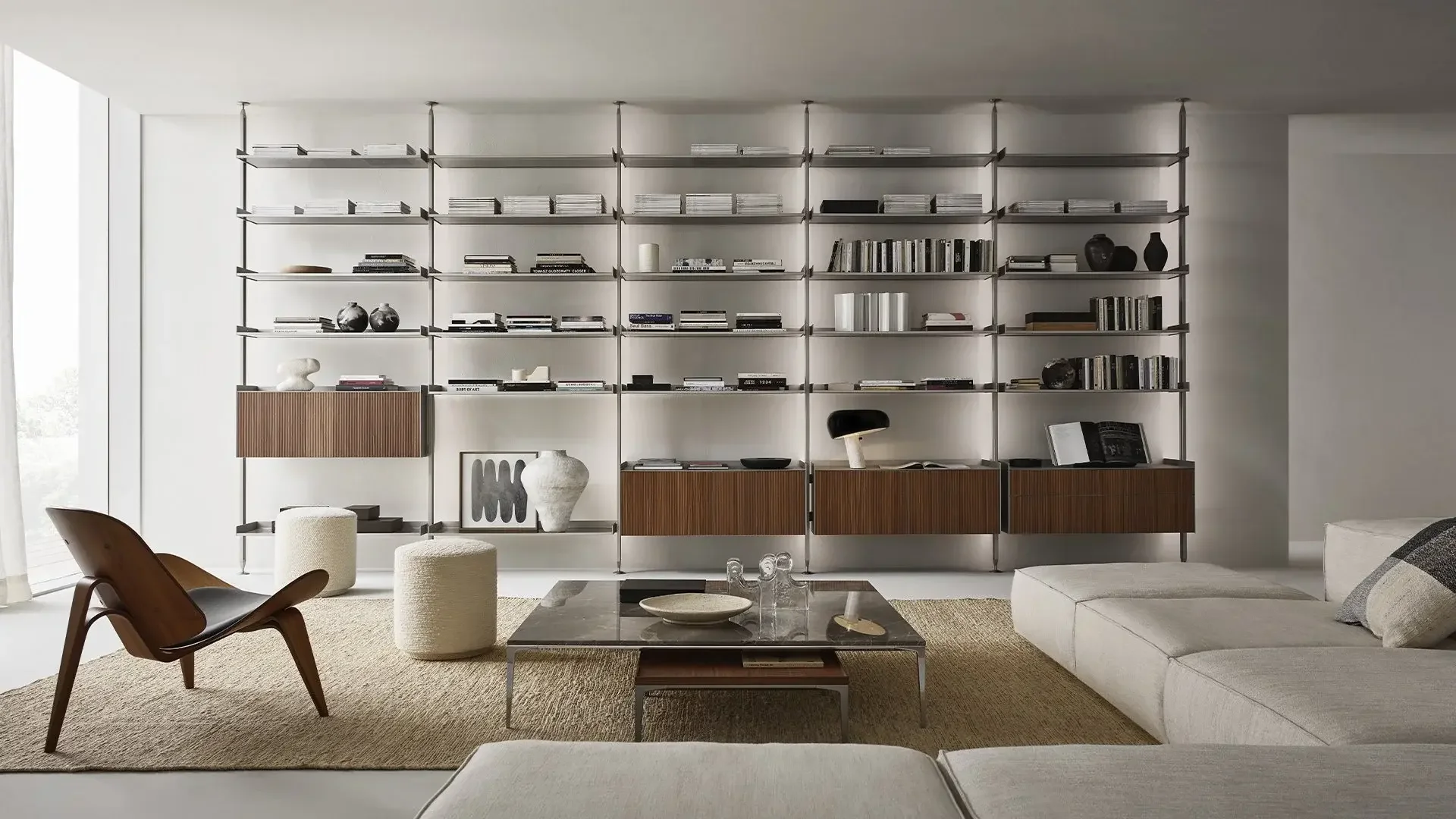 Modern living room with Rimadesio built-in bookshelf, beige sofa, wooden chair, and coffee table, decorated with vases and art pieces.