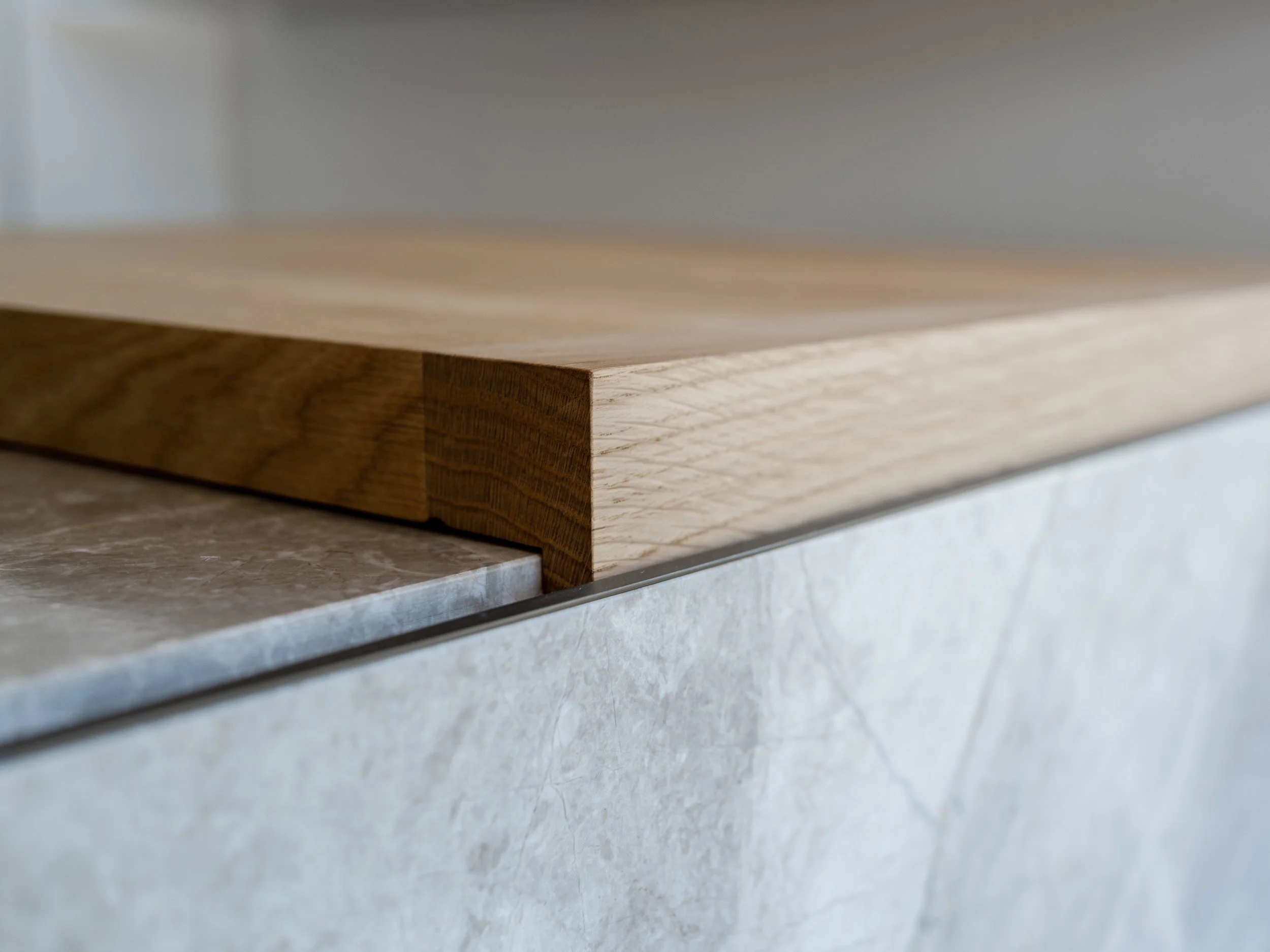 Close-up detail of a contemporary kitchen island featuring a light oak breakfast bar expertly joined to a grey porcelain worktop.