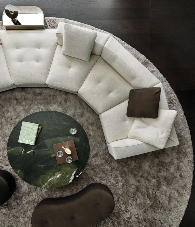 Top-down view of Minotti sofa composition with curved cream sofa, black round coffee table, dark brown ottoman, and circular gray rug, designed by Abitalia South Coast in the United Kingdom
