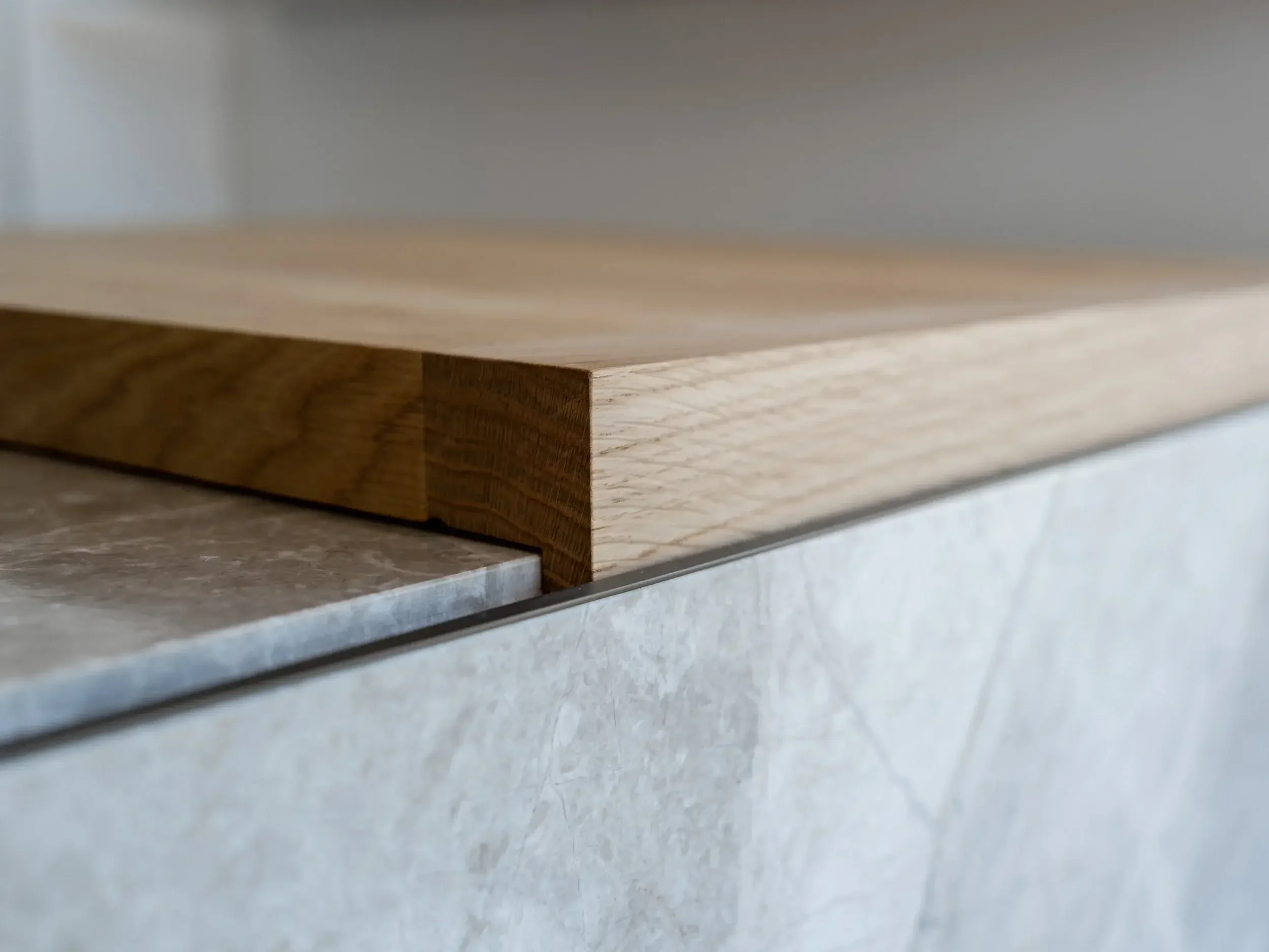 Close-up detail of a contemporary kitchen island featuring a light oak breakfast bar expertly joined to a grey porcelain worktop.