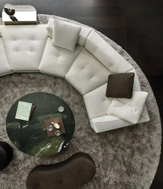 Top-down view of Minotti sofa composition with curved cream sofa, black round coffee table, dark brown ottoman, and circular gray rug, designed by Abitalia South Coast in the United Kingdom