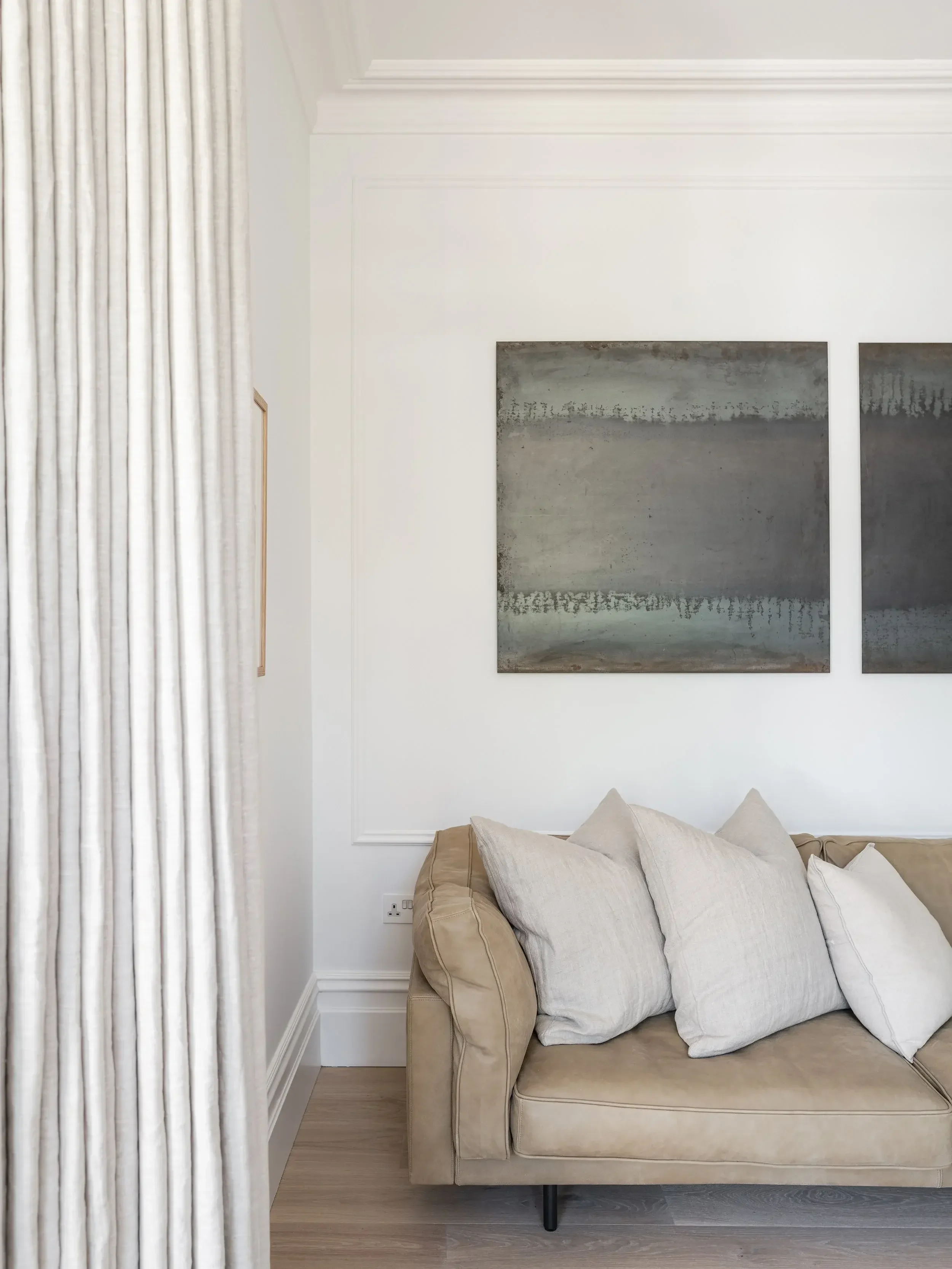 Modern interior design in Poole featuring a neutral leather sofa with linen cushions, minimalist wall molding, and abstract contemporary artwork.