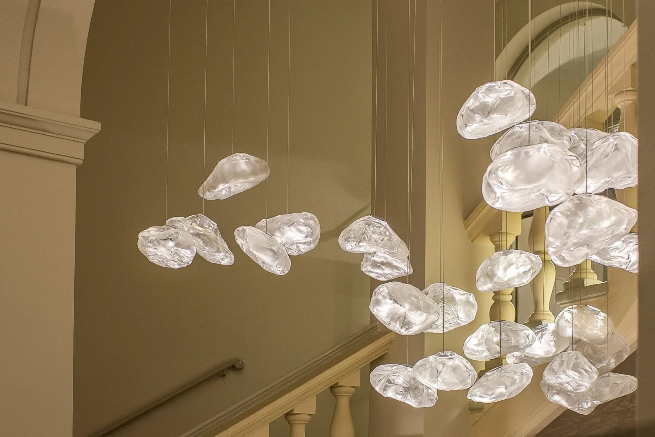 A modern chandelier with multiple irregularly shaped glass or acrylic bulbs hanging over a staircase in a building interior.