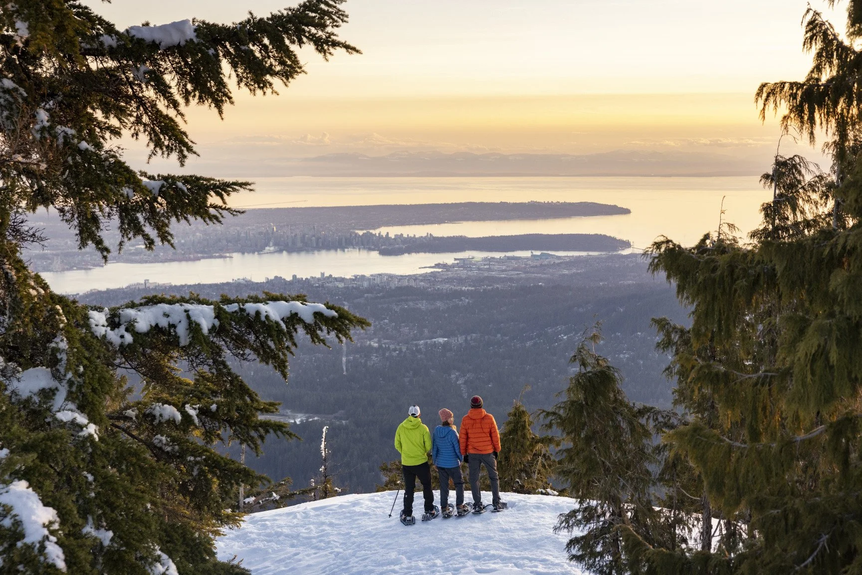 3 hikers overlooking downtown Vancouver at sunset while snowshoeing