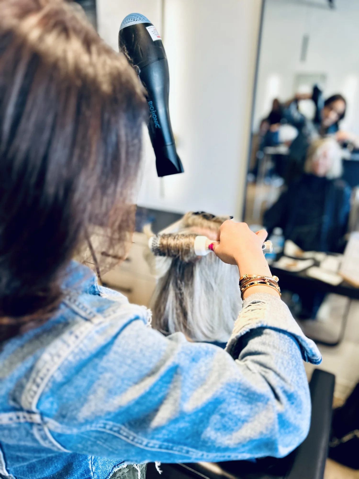 Stylist blow-drying and rounding a client's hair in the salon