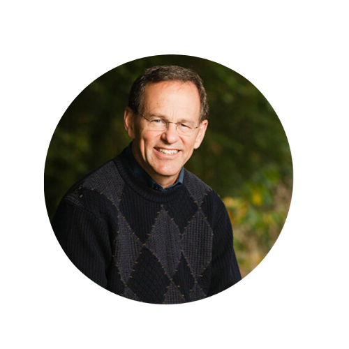 Smiling man with glasses wearing a dark argyle sweater outdoors