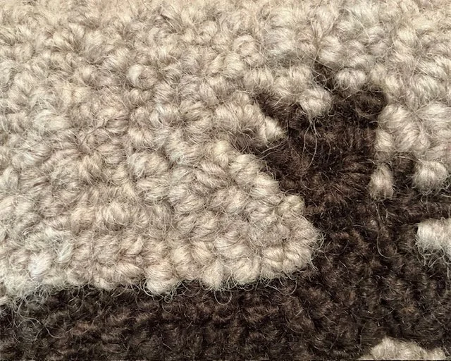 Close-up of hand-hooked wool loops in brown and slate, showing dense texture and fiber variation.