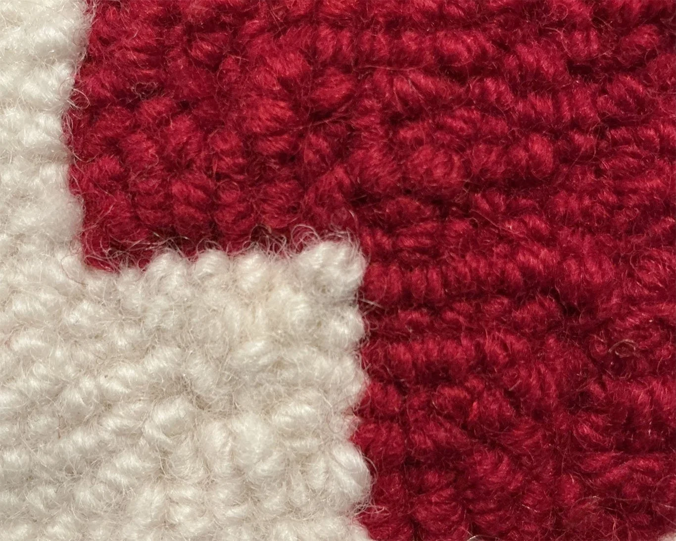 Close-up of hand-hooked wool loops in red and ivory, showing dense texture and fiber variation.