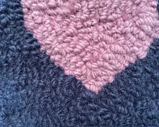 Close-up of hand-hooked wool loops in indigo and pink, showing dense texture and fiber variation.