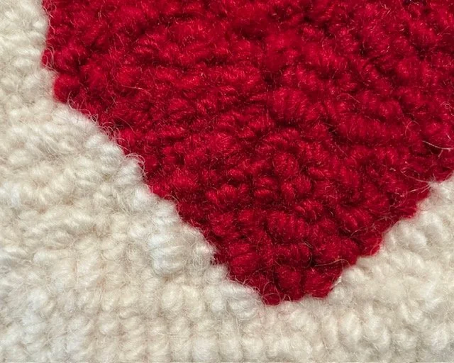 Close-up of hand-hooked wool loops in ivory and red, showing dense texture and fiber variation.