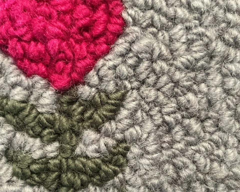 Close-up of hand-hooked wool loops in slate, bright pink, and green,, showing dense texture and fiber variation.
