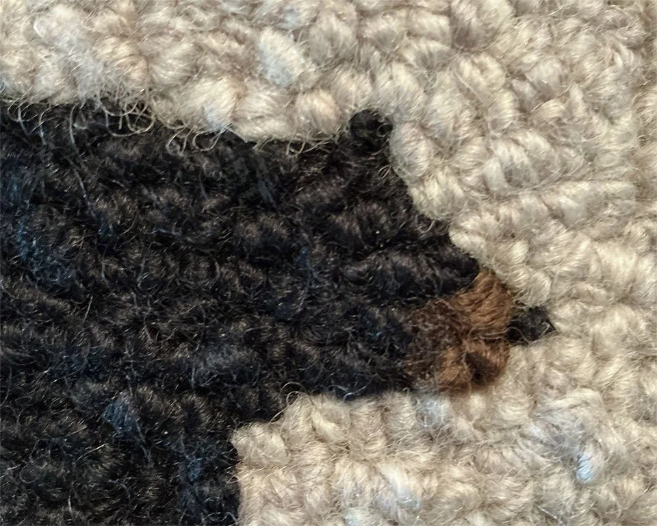 Close-up of hand hoked wool loops in black and granite, showing dense texture and fiber variation.