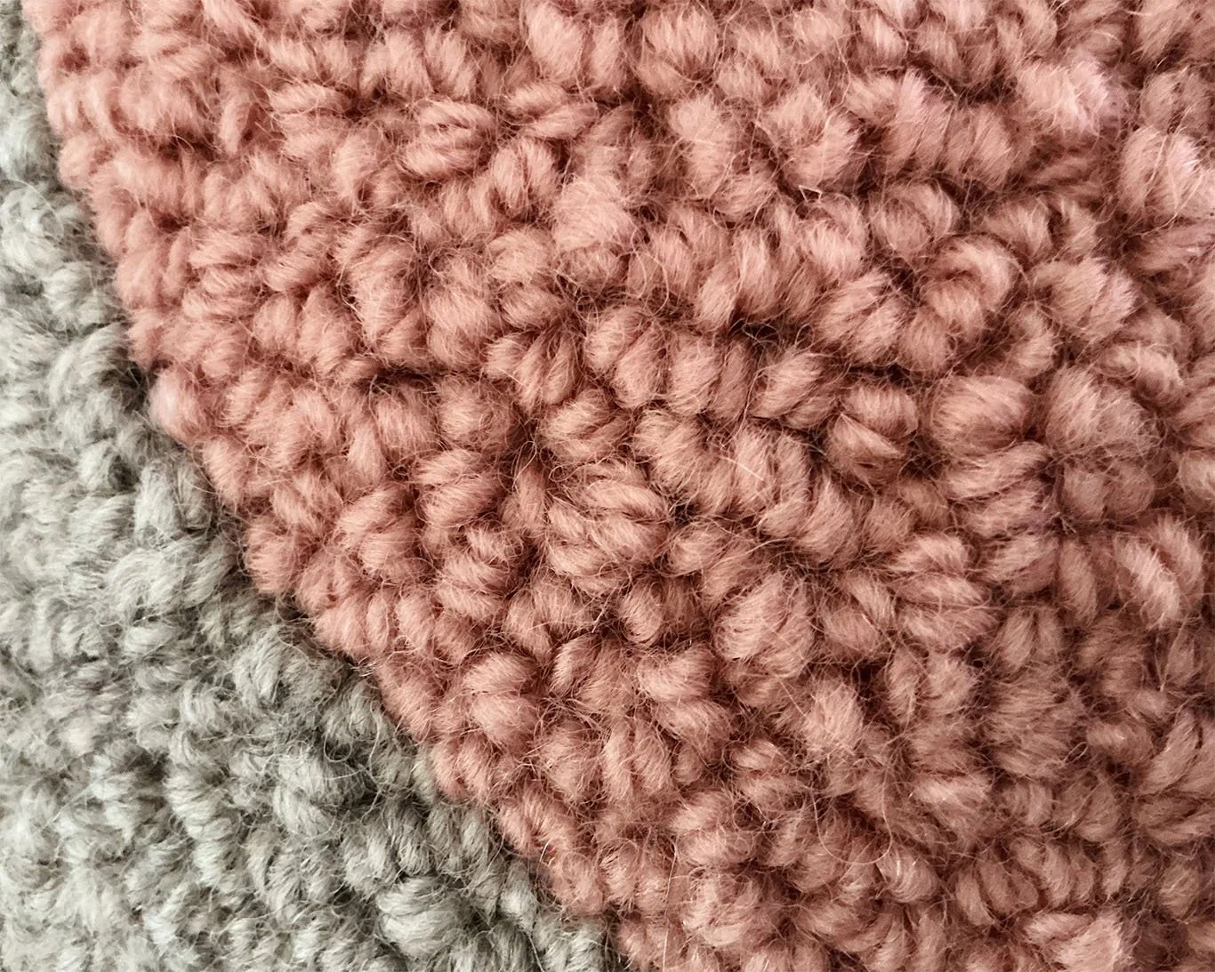 Close-up of hand-hooked wool loops showing blush heart against stone-gray wool fibers.