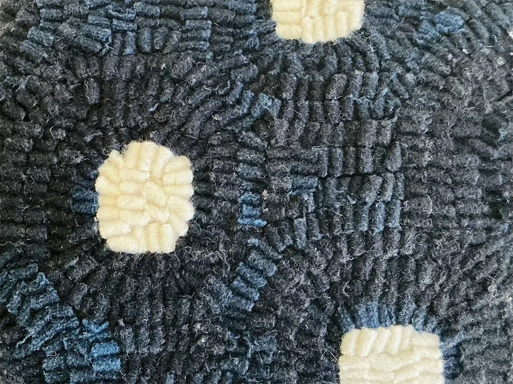 Detail of hand-hooked wool forming dot motif on deep navy ground.