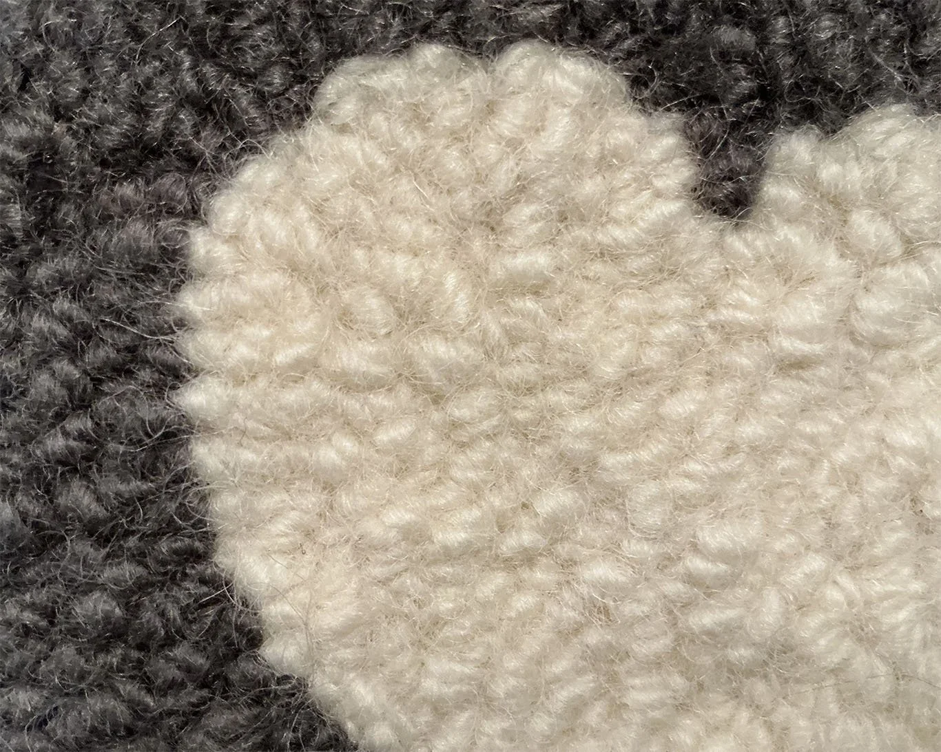 Close-up of hand-hooked wool loops in slate and ivory, showing dense texture and fiber variation.