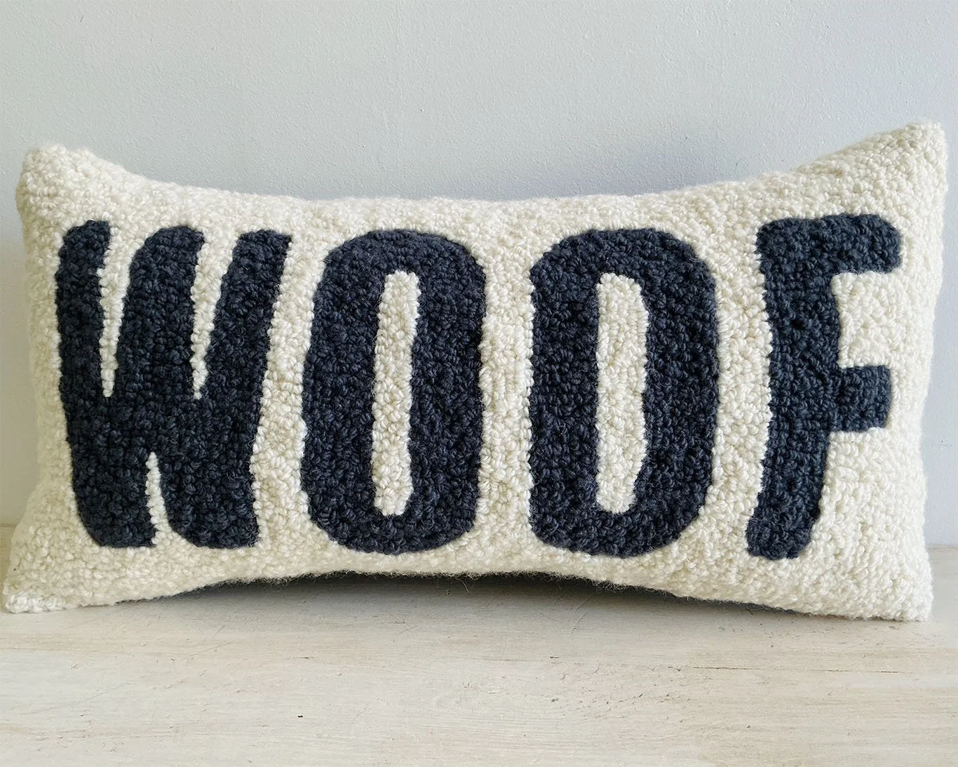 Hand-hooked wool pillow with the word "WOOF" in slate lettering on a bone-colored wool background.
