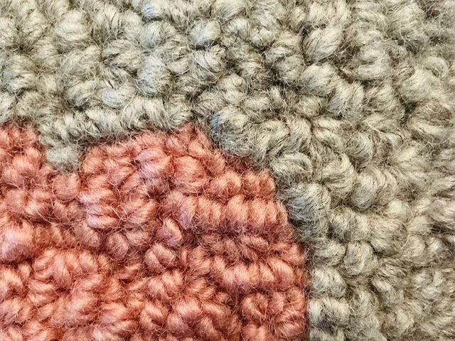 Detail of hand-hooked wool loops showing blush-pink heart against stone-gray wool fibers.