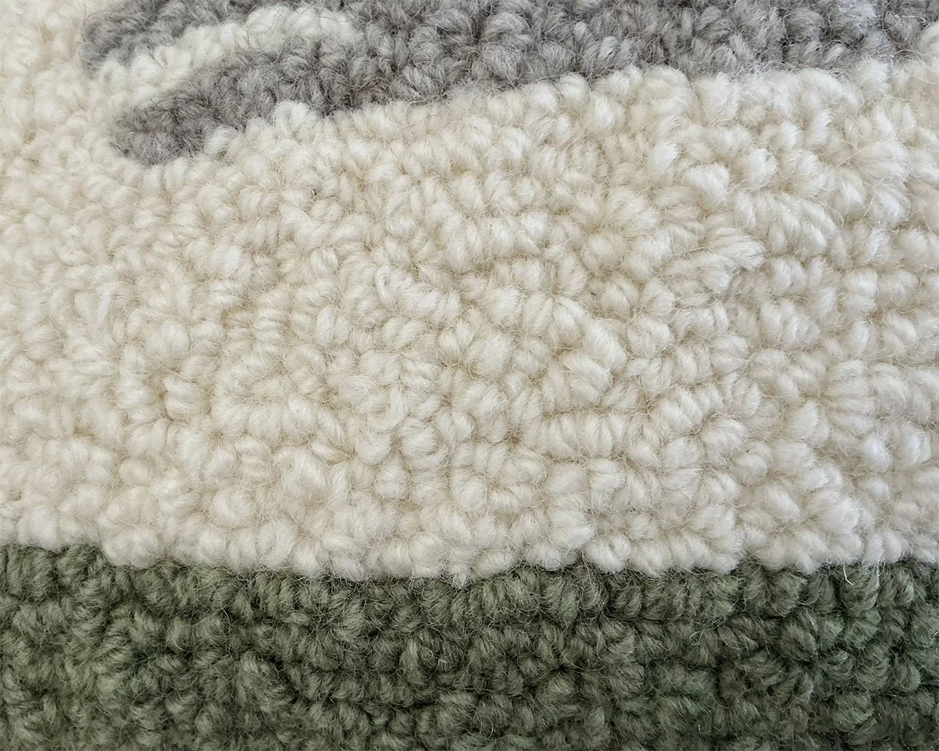 Detail of hand-hooked wool showing the rabbit, green ground band, and ivory field.
