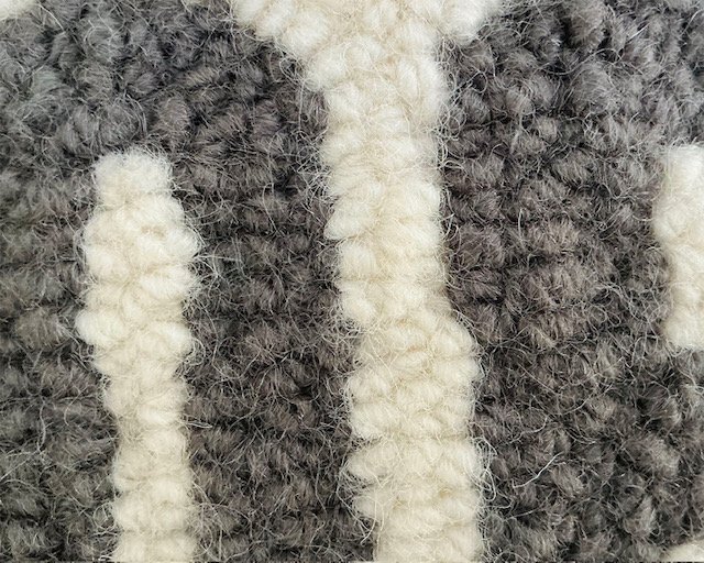 Detail of hand-hooked wool showing charcoal lettering against the natural ground.