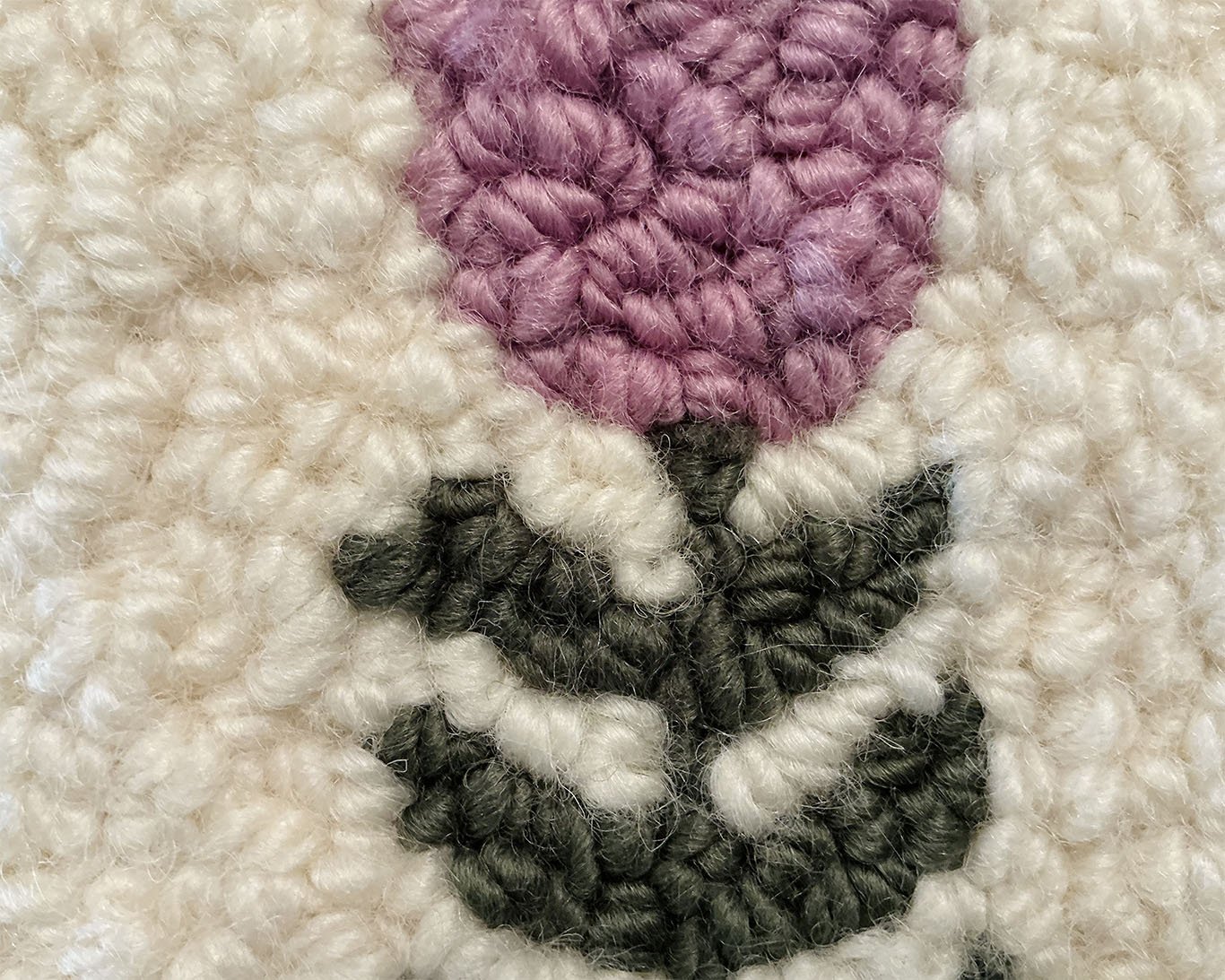 Close-up of hand-hooked wool loops in ivory, lavender, and green, showing dense texture and fiber variation.