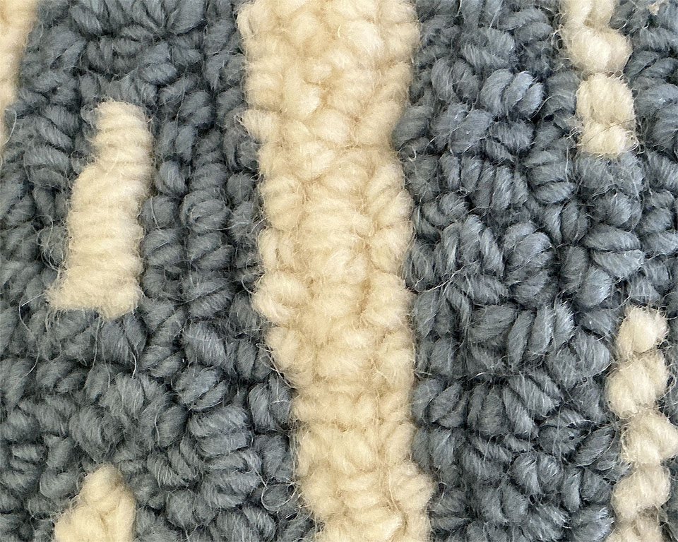 Detail of hand-hooked wool showing blue lettering against the ivory ground.