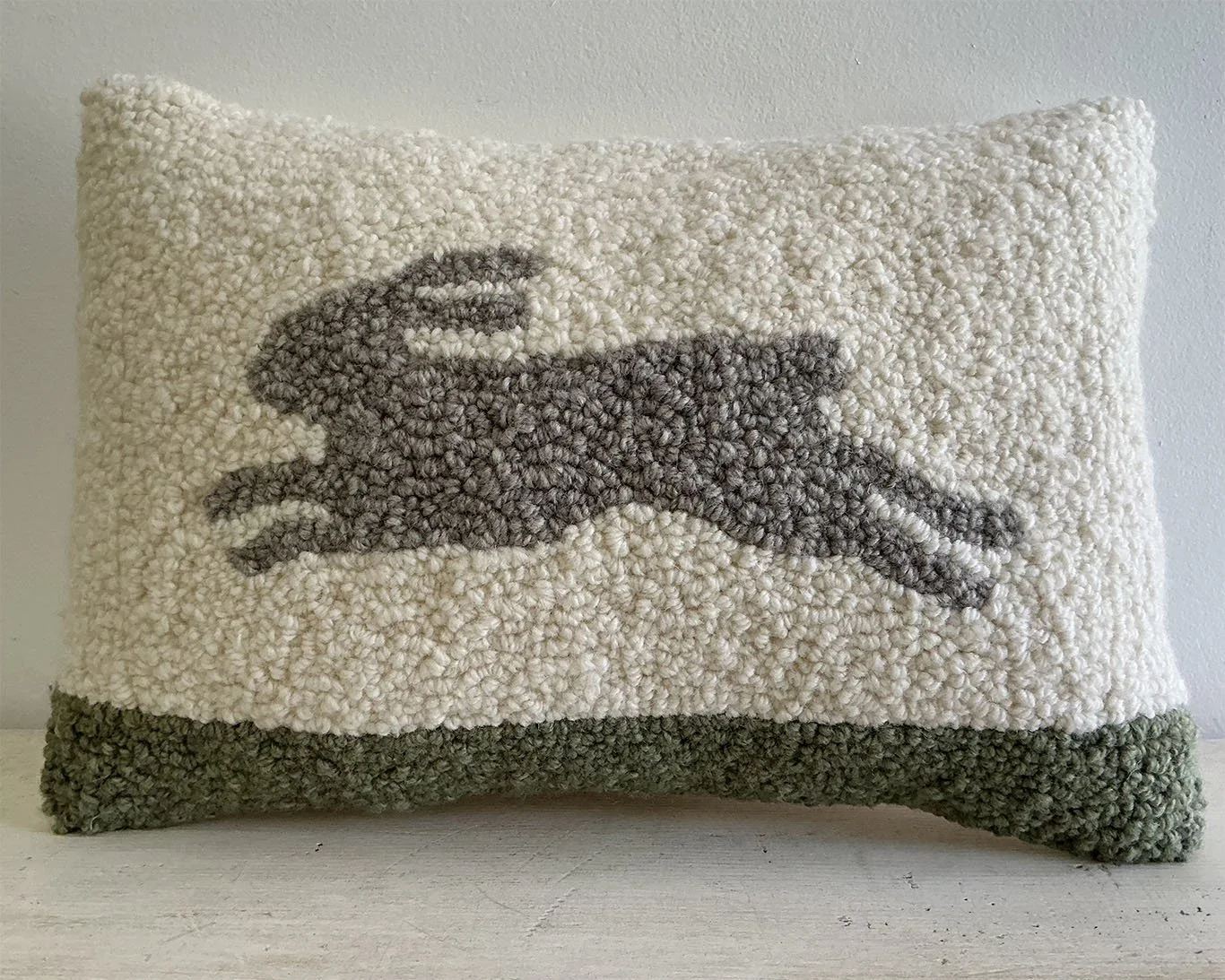 Ivory hand-hooked wool pillow with a running rabbit above a green ground band.