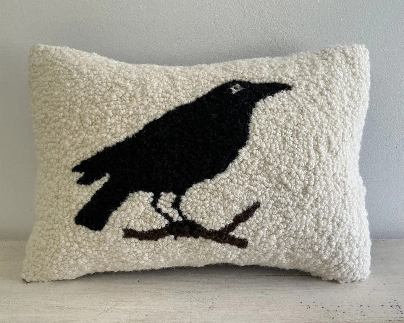 Ivory hand-hooked wool pillow with a black crow perched on a branch.
