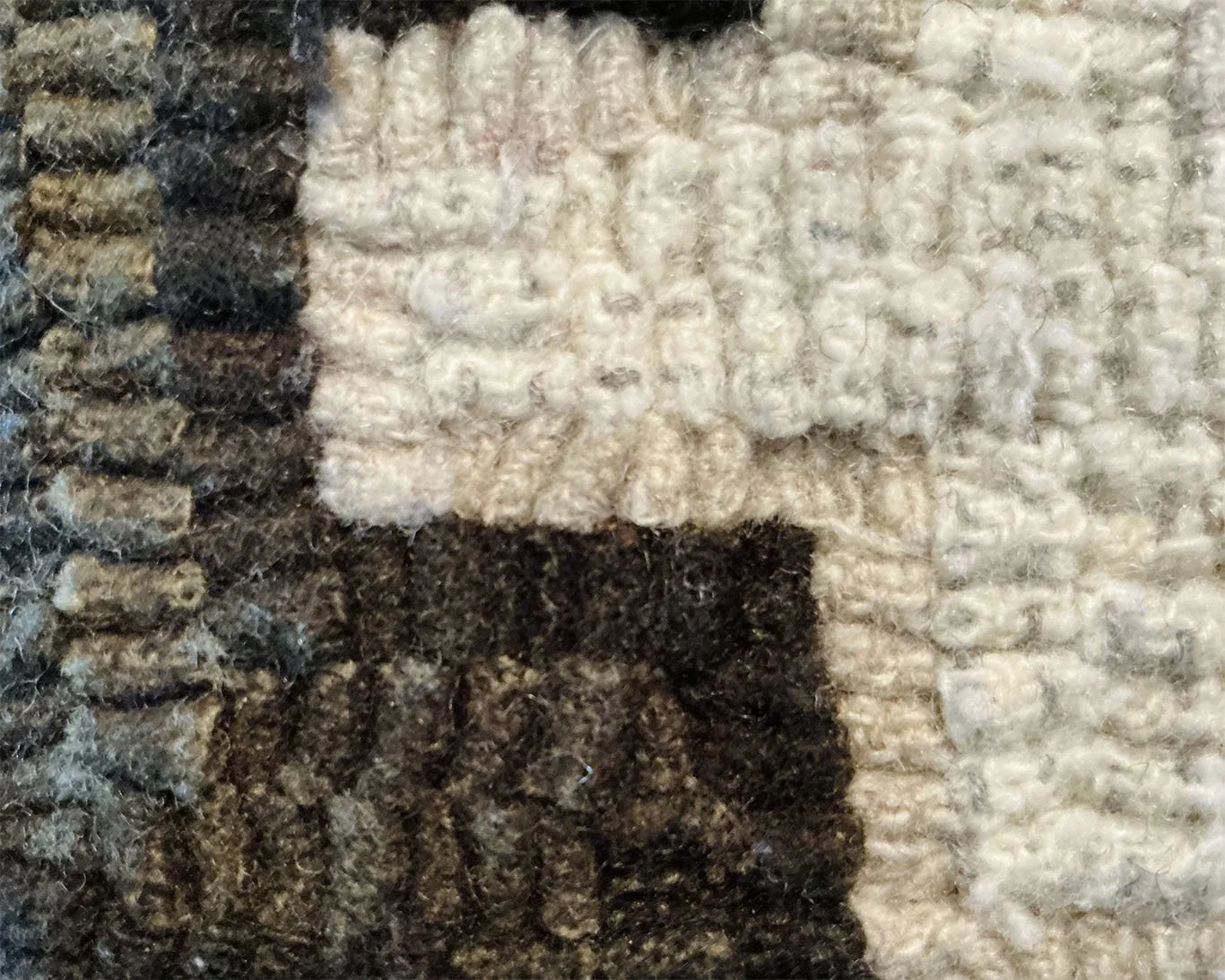 Detail of hand-hooked wool loops showing ivory cross against mottled loden wool fibers.