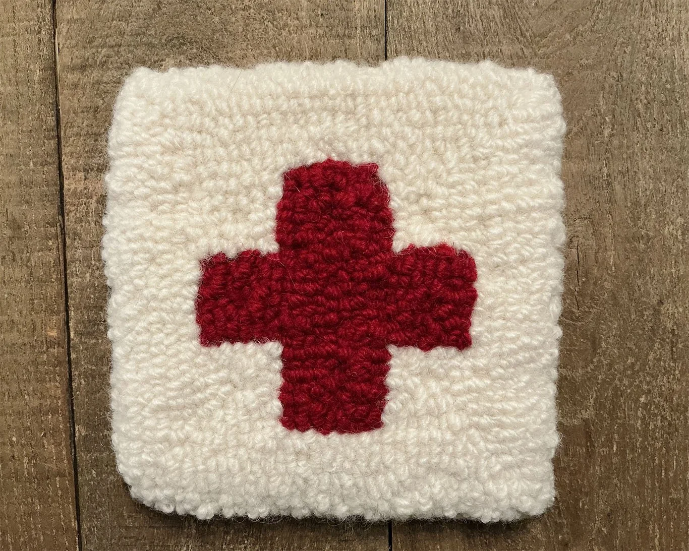 Hand-hooked wool panel in ivory featuring centered red cross in square format.