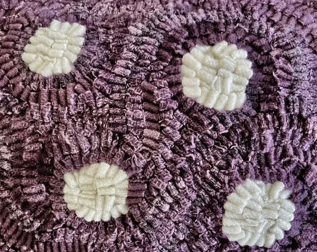 Detail of hand-hooked wool forming a dot motif on plum ground.