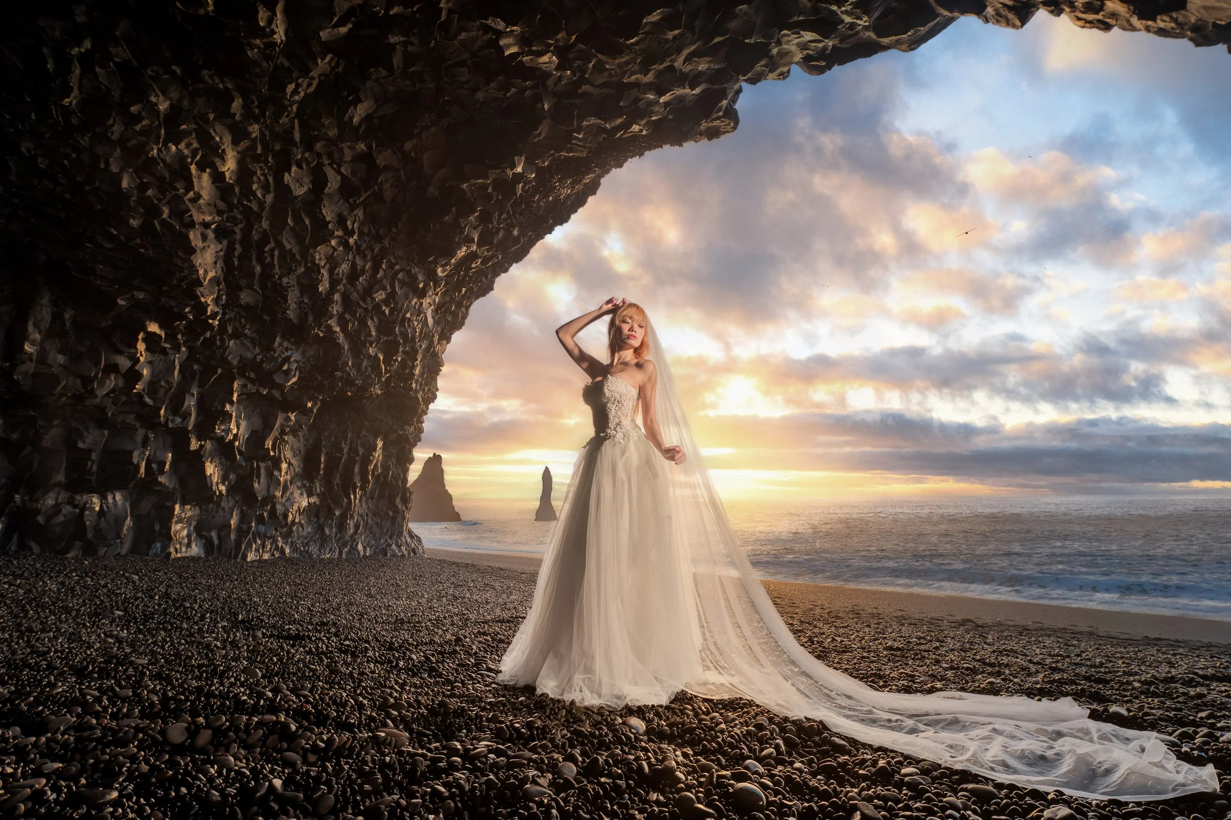Bride in white gown standing under the basalt cave arch