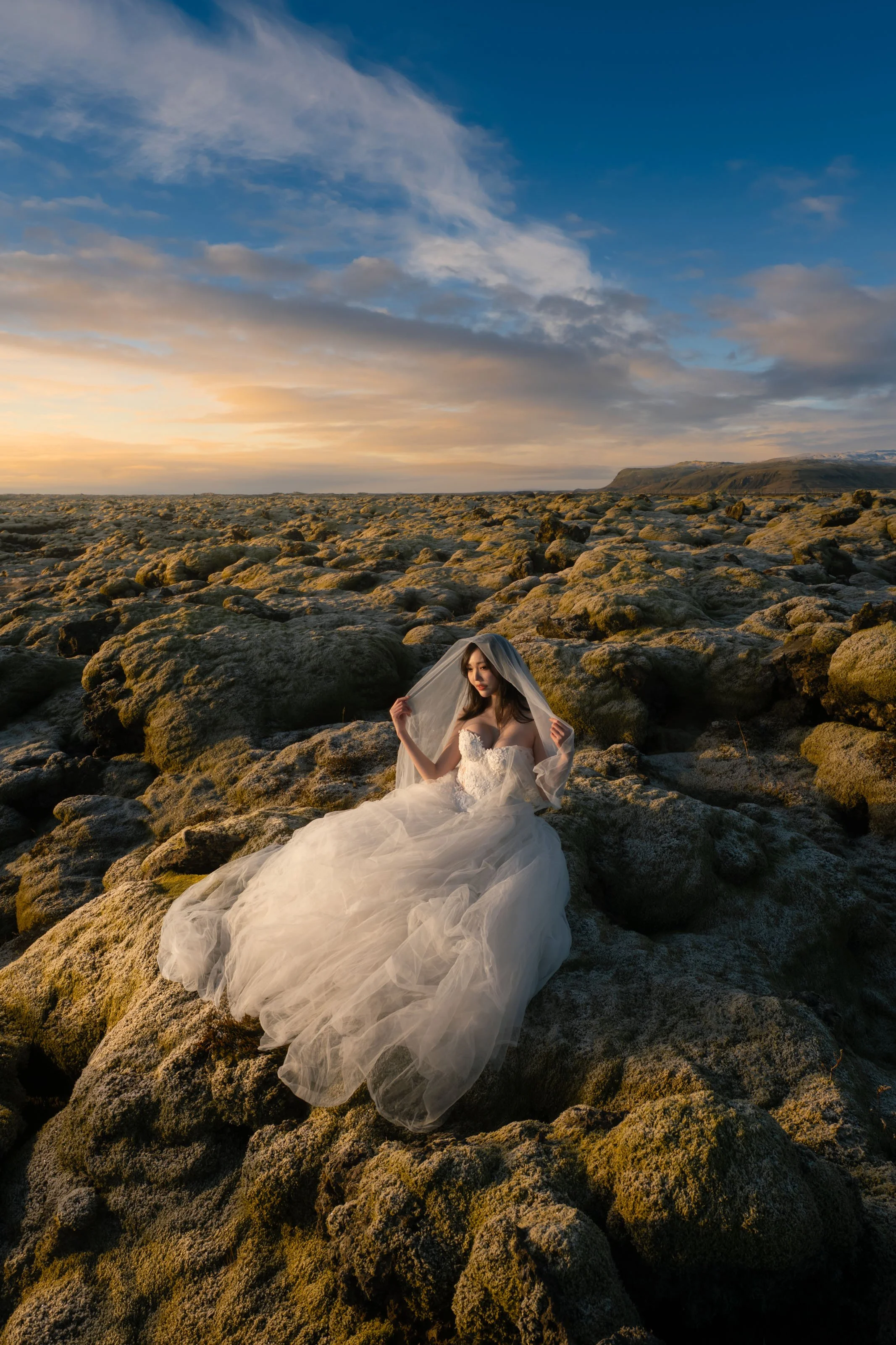 Bride sitting gracefully on the moss-covered lava rocks