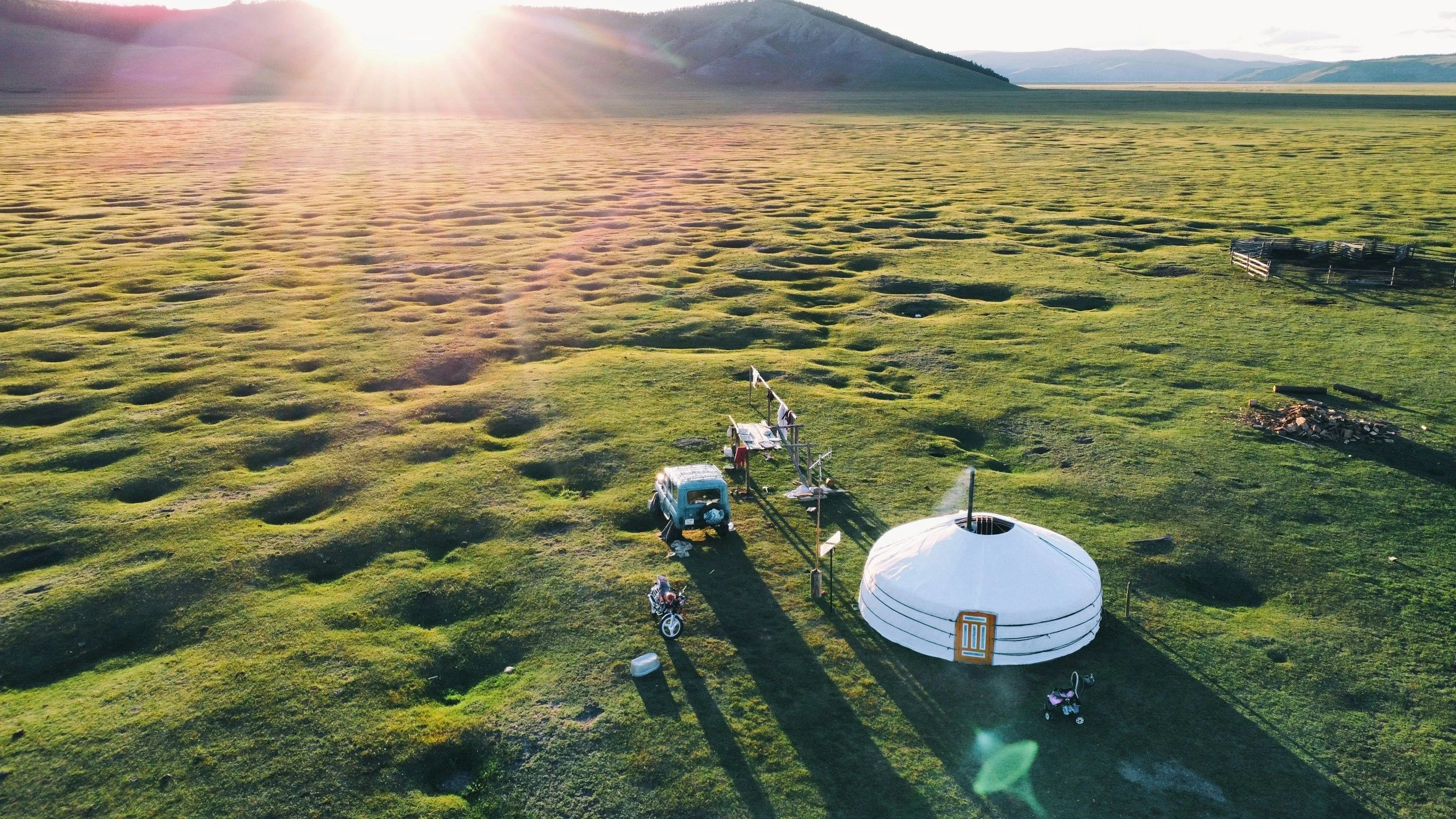 Aerial view of a traditional Mongolian Ger camp and vintage van at sunset with the Khangai Mountains in the background