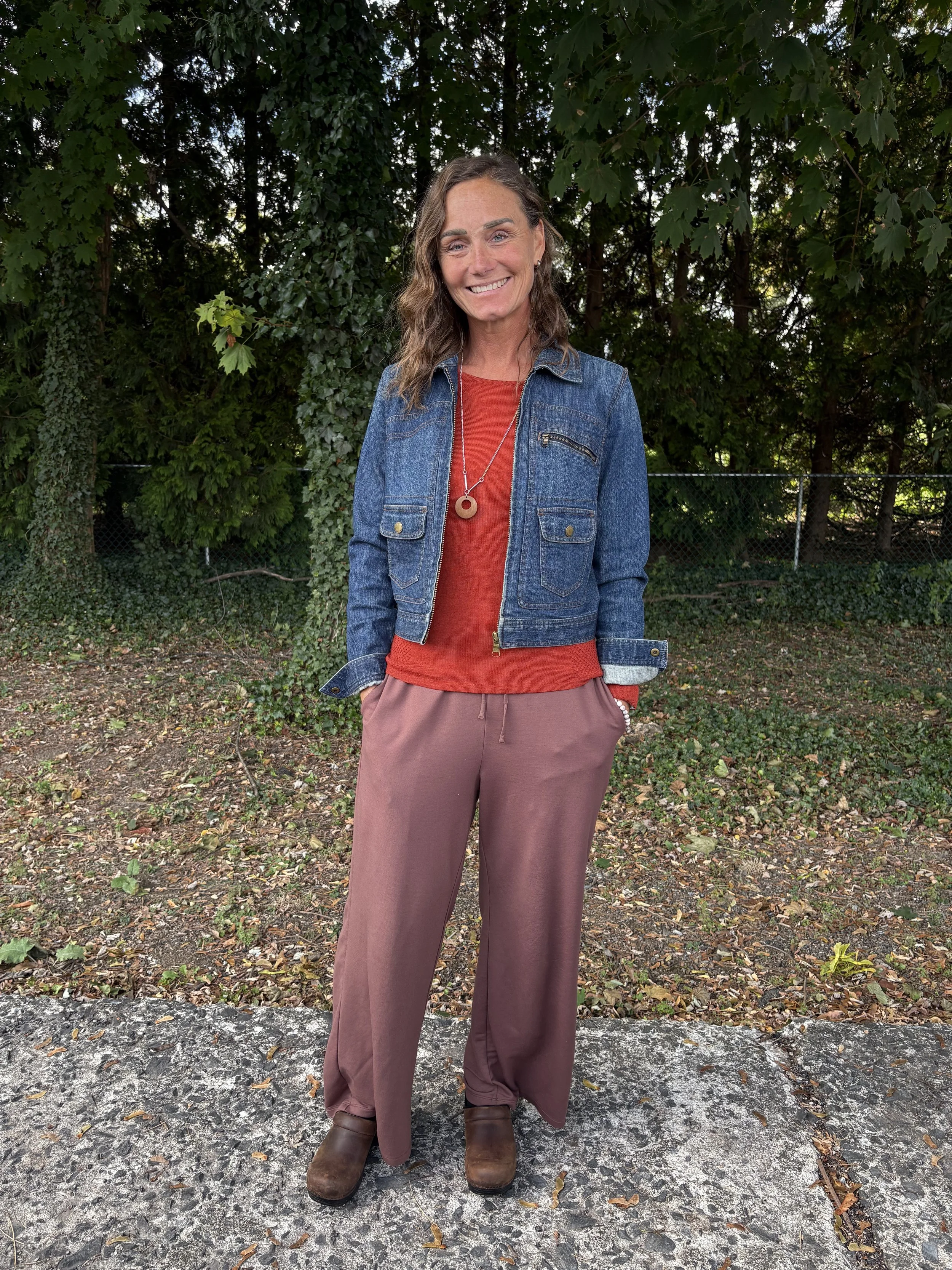 Anne Rankin a certified trauma informed graduate student counselor intern standing in tree line smiling. at the camera