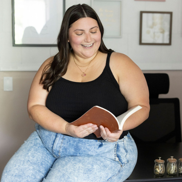 Jess fry therapist reading a body image book sitting on a desk smiling