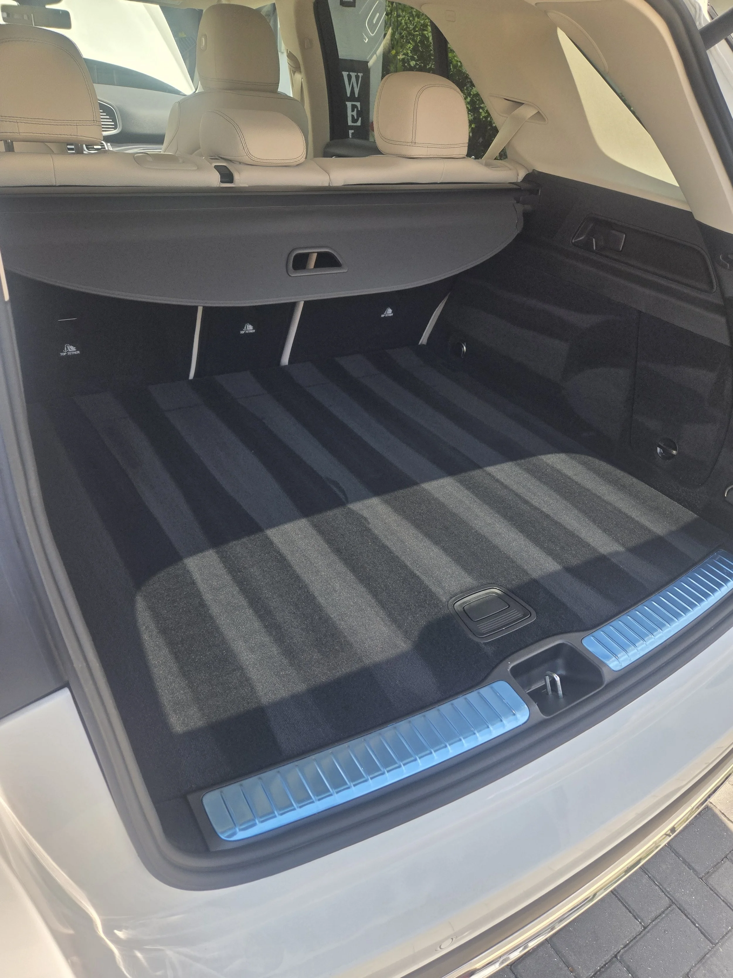 The image shows the open trunk of a car, revealing a spacious cargo area with a black and gray striped floor mat. The beige interior seating is visible in the background, along with the headrests and the rear windshield.